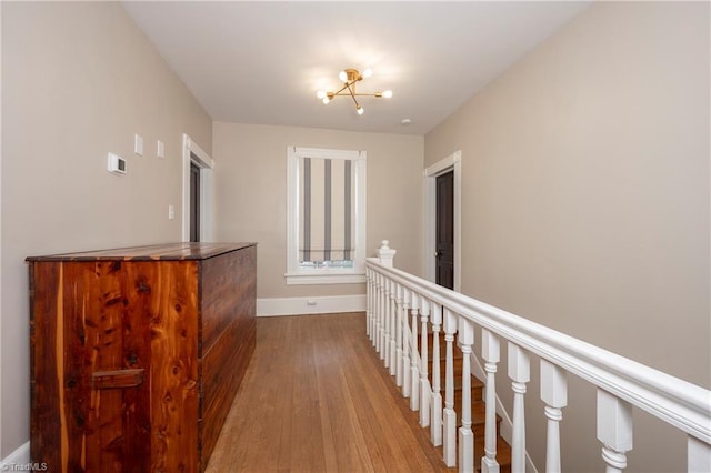 corridor featuring baseboards, wood finished floors, and an upstairs landing