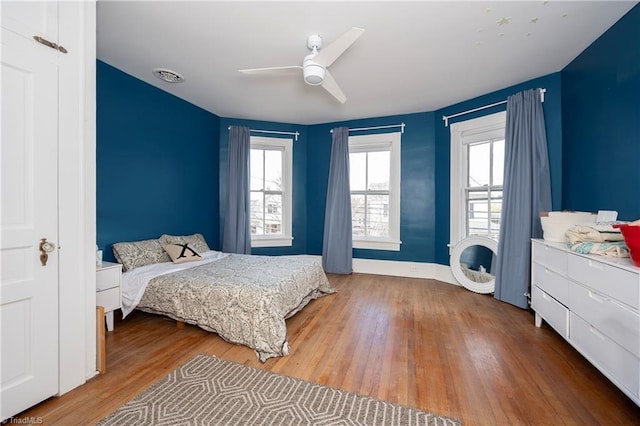 bedroom featuring a ceiling fan, multiple windows, visible vents, and wood finished floors