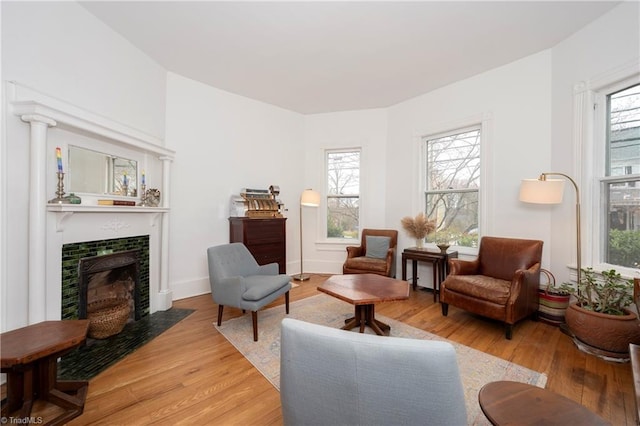 sitting room with light wood-style floors, plenty of natural light, baseboards, and a tiled fireplace