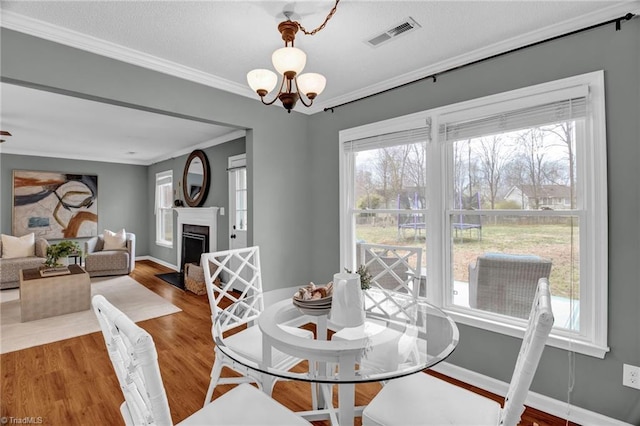 dining room featuring wood finished floors, visible vents, a fireplace, ornamental molding, and a notable chandelier