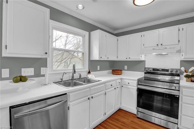 kitchen with under cabinet range hood, a sink, white cabinetry, appliances with stainless steel finishes, and crown molding