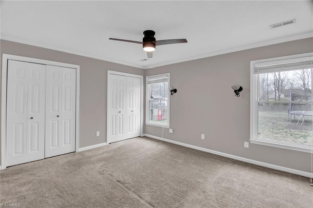 unfurnished bedroom featuring visible vents, two closets, carpet, crown molding, and baseboards