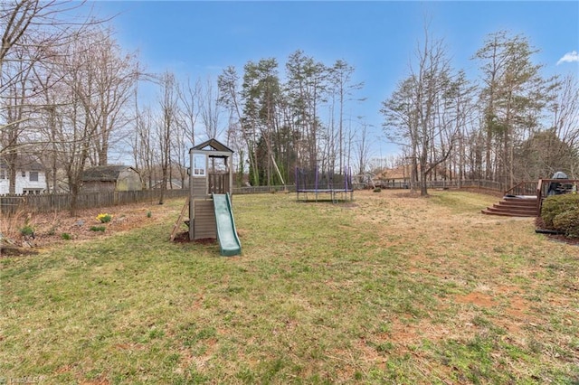 view of yard with a wooden deck, fence, a trampoline, and a playground