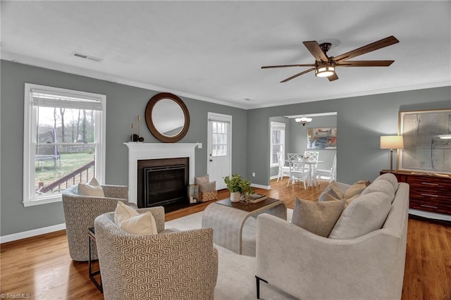 living area featuring crown molding, wood finished floors, visible vents, and a healthy amount of sunlight