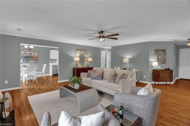 living area with a ceiling fan, wood finished floors, baseboards, and ornamental molding