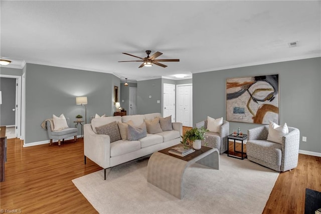 living room featuring visible vents, light wood-style flooring, baseboards, and ornamental molding