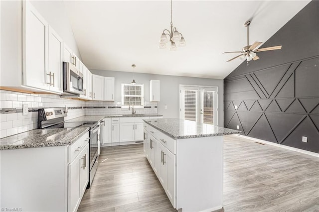 kitchen featuring a kitchen island, vaulted ceiling, light wood-style flooring, appliances with stainless steel finishes, and a sink