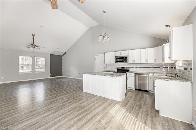 kitchen with light stone countertops, a sink, light wood-style floors, appliances with stainless steel finishes, and open floor plan