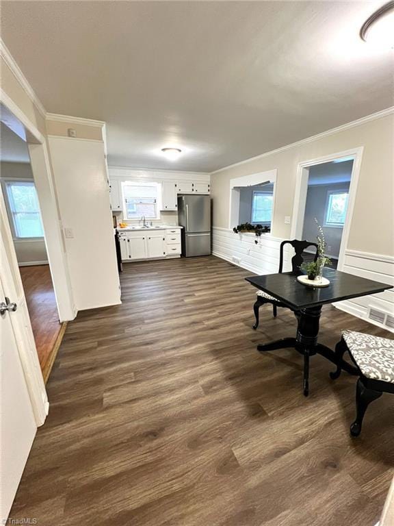 kitchen with a wealth of natural light, dark wood-type flooring, crown molding, white cabinets, and stainless steel refrigerator