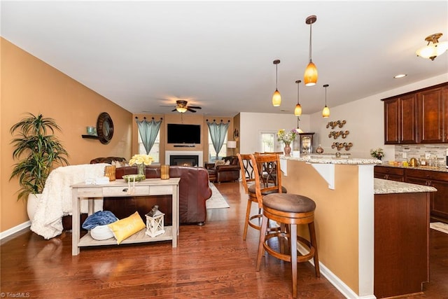 2711 Chari Park Ln, Walkertown, NC 27051 - kitchen with a ceiling fan, a kitchen breakfast bar, dark wood finished floors, a warm lit fireplace, and baseboards