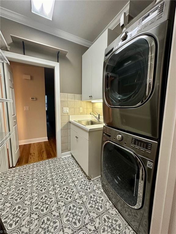 clothes washing area with sink, light hardwood / wood-style floors, crown molding, cabinets, and stacked washer and dryer