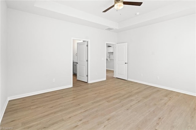 unfurnished bedroom with a spacious closet, light hardwood / wood-style flooring, ceiling fan, and a tray ceiling