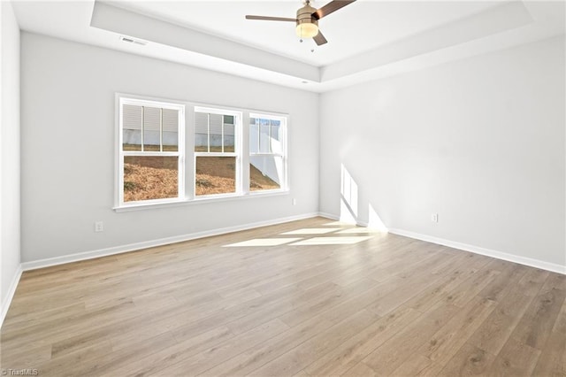 unfurnished room featuring a tray ceiling, ceiling fan, and light wood-type flooring