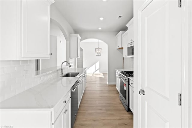 kitchen featuring appliances with stainless steel finishes, sink, white cabinets, light stone countertops, and light wood-type flooring