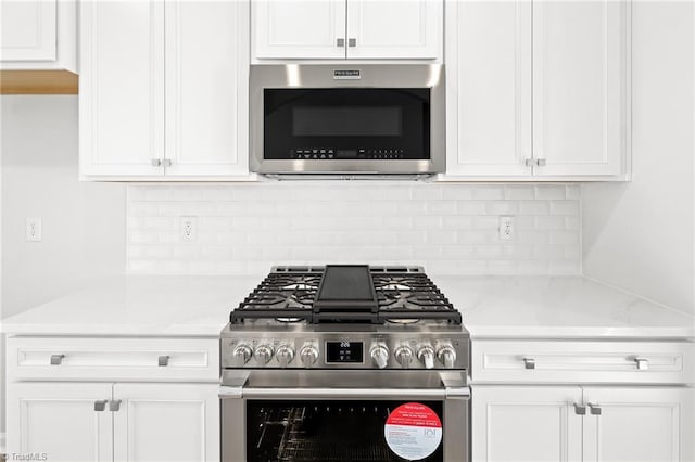 kitchen featuring white cabinetry, appliances with stainless steel finishes, light stone countertops, and backsplash