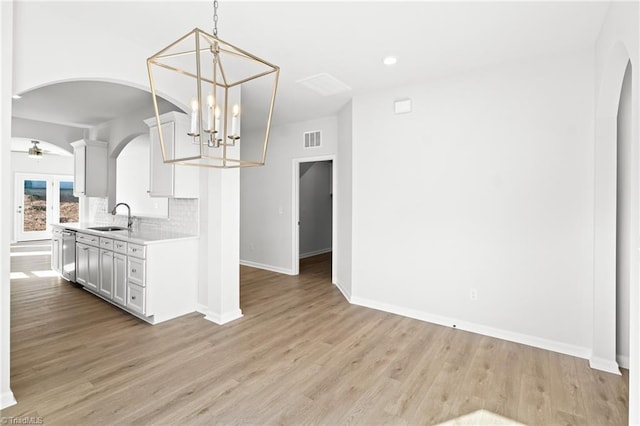 kitchen with sink, decorative backsplash, decorative light fixtures, stainless steel dishwasher, and light wood-type flooring