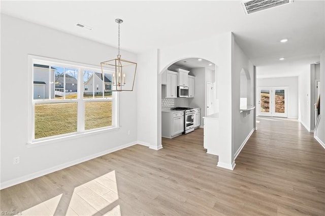 unfurnished dining area with a notable chandelier, a wealth of natural light, and light hardwood / wood-style floors