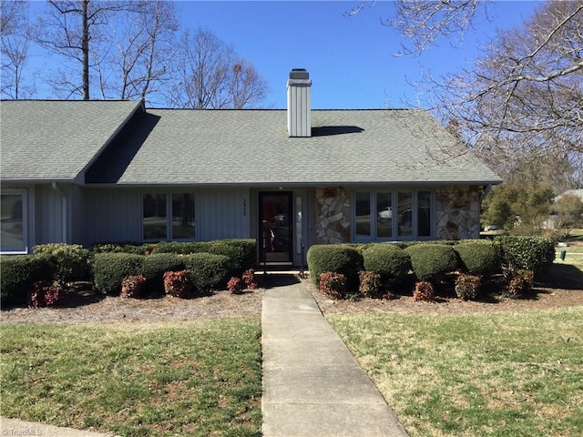 view of front of home with stone siding, a shingled roof, a chimney, and a front yard