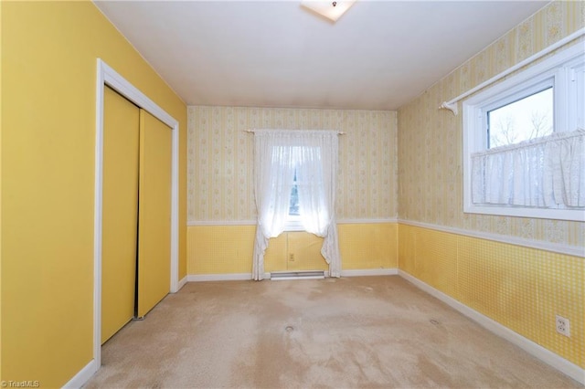 unfurnished room featuring wallpapered walls, baseboards, light carpet, baseboard heating, and wainscoting