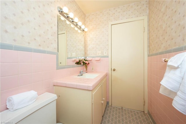 bathroom featuring tile walls, a wainscoted wall, wallpapered walls, and vanity