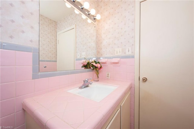 bathroom with wallpapered walls, tile walls, vanity, and wainscoting