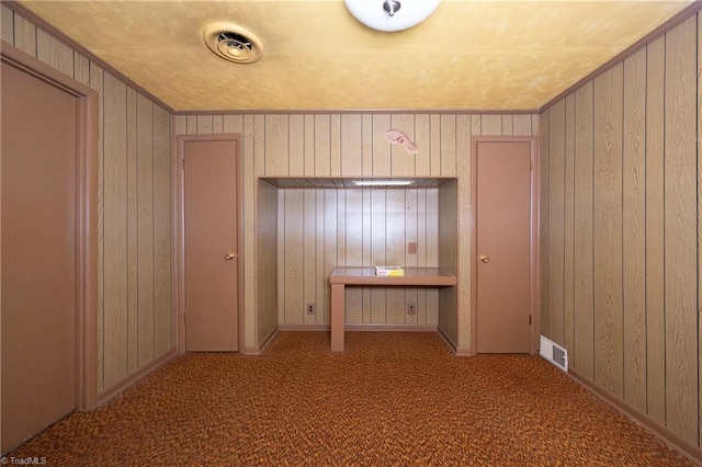 unfurnished bedroom with visible vents, carpet, ornamental molding, and wooden walls