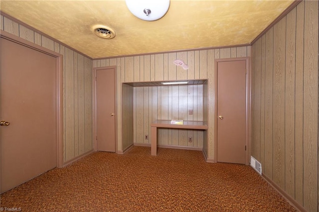 interior space with carpet flooring, visible vents, wood walls, and ornamental molding