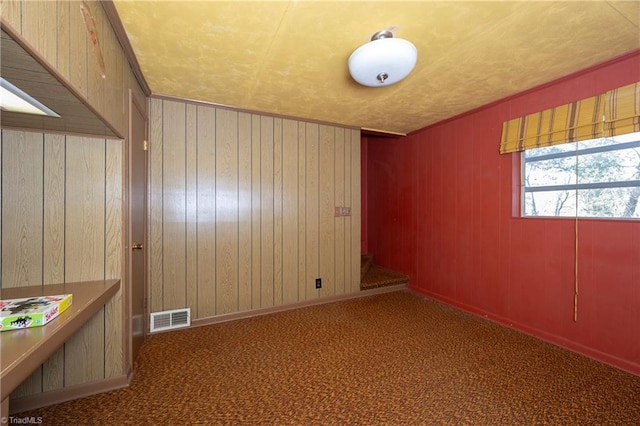 spare room featuring visible vents, carpet, and wood walls