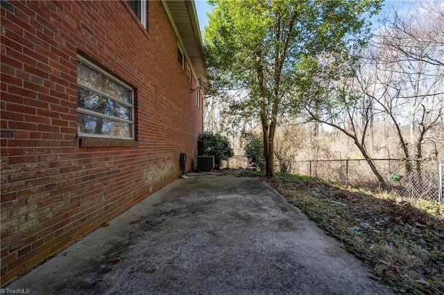 view of side of home featuring brick siding, central AC unit, and fence