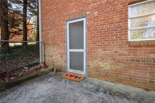 doorway to property featuring brick siding and fence