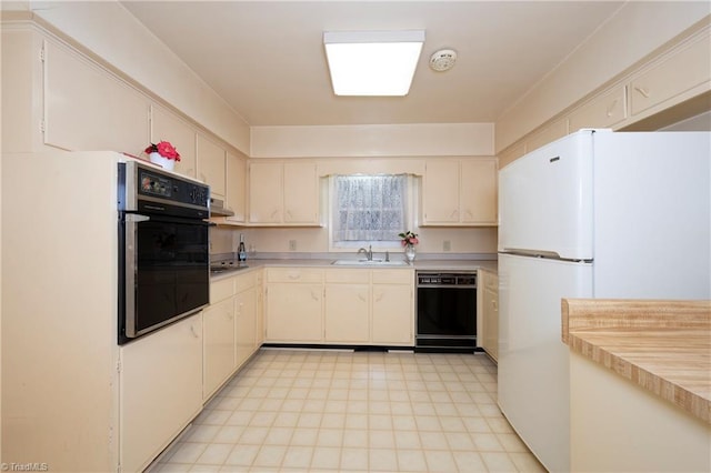 kitchen with a sink, black appliances, light countertops, under cabinet range hood, and cream cabinets