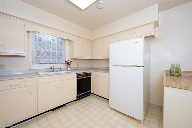 kitchen with a sink, black dishwasher, light countertops, and freestanding refrigerator