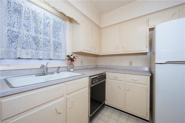 kitchen with a sink, dishwasher, light countertops, and freestanding refrigerator