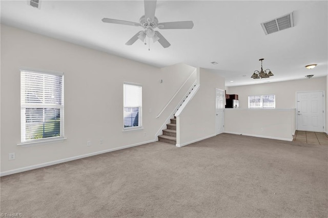 unfurnished living room with ceiling fan with notable chandelier, plenty of natural light, and light carpet