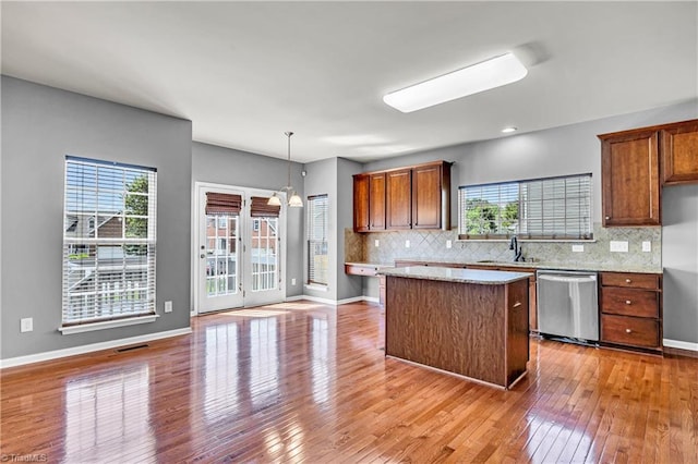 kitchen featuring light wood finished floors, a sink, dishwasher, a kitchen island, and tasteful backsplash