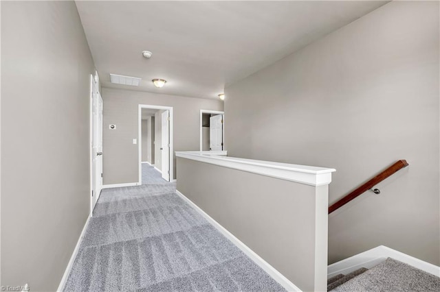 corridor with visible vents, an upstairs landing, baseboards, and carpet floors