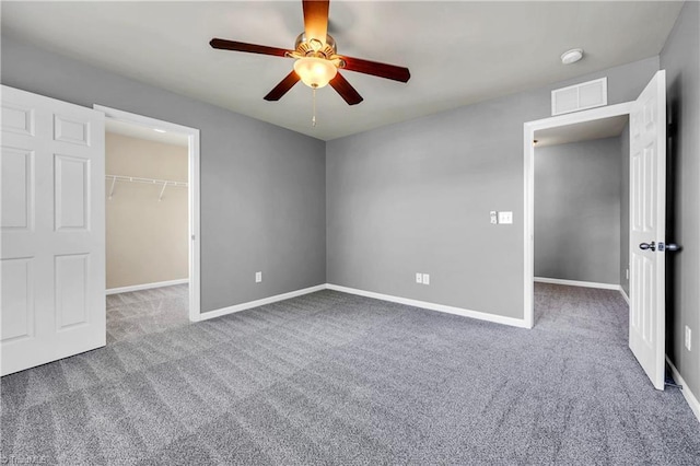 unfurnished bedroom featuring a ceiling fan, a walk in closet, carpet floors, visible vents, and baseboards