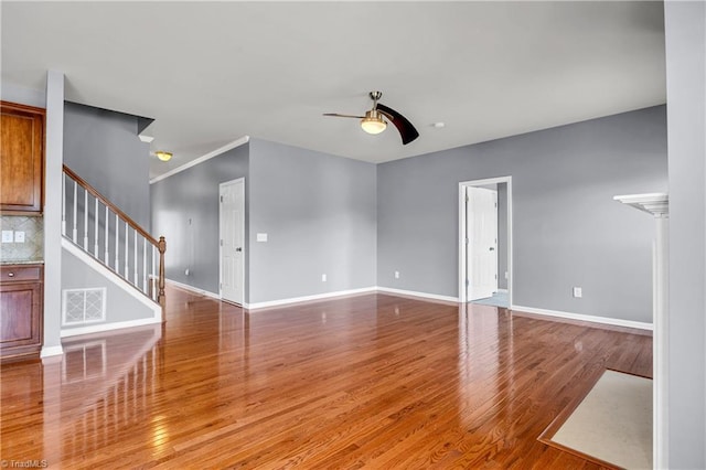 unfurnished living room with stairs, wood finished floors, visible vents, ceiling fan, and baseboards