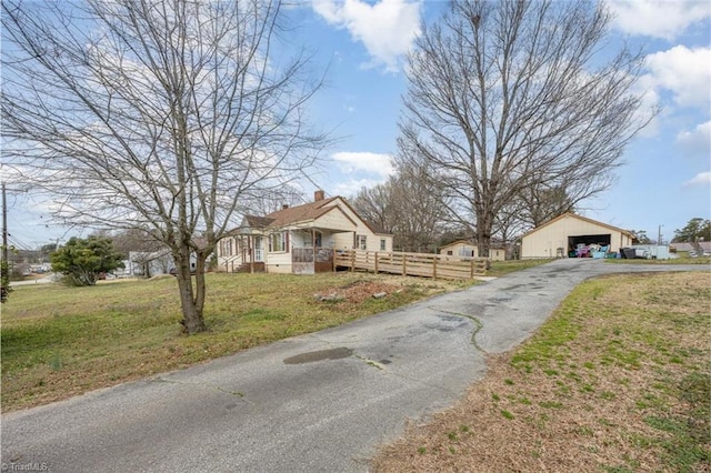 view of front of house with an outbuilding, fence, a chimney, a front lawn, and a garage