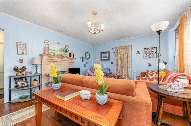 living room featuring a notable chandelier, a textured ceiling, wood finished floors, a fireplace, and crown molding