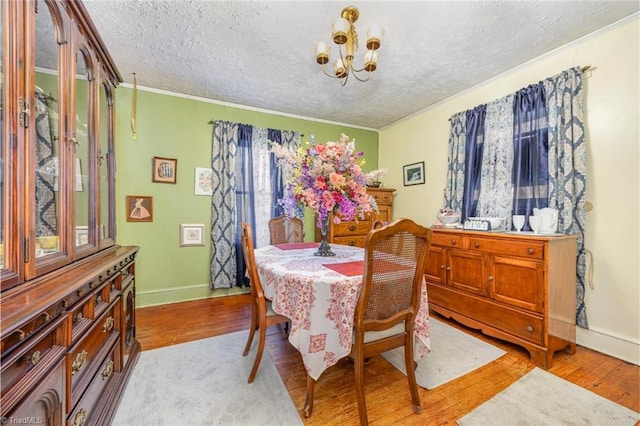 dining space featuring a notable chandelier, light wood-style floors, baseboards, and a textured ceiling