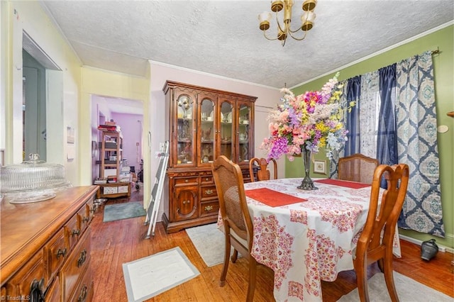 dining room with a textured ceiling, light wood-style flooring, ornamental molding, and a chandelier