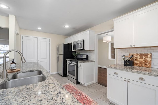 kitchen featuring appliances with stainless steel finishes, decorative light fixtures, sink, white cabinets, and light stone counters