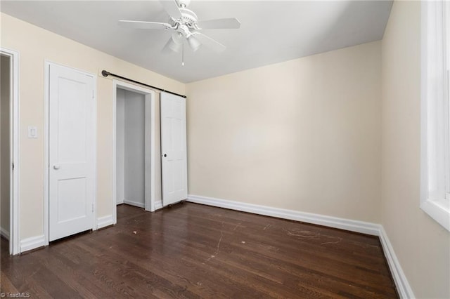 unfurnished bedroom with a barn door, dark wood-type flooring, ceiling fan, and a closet