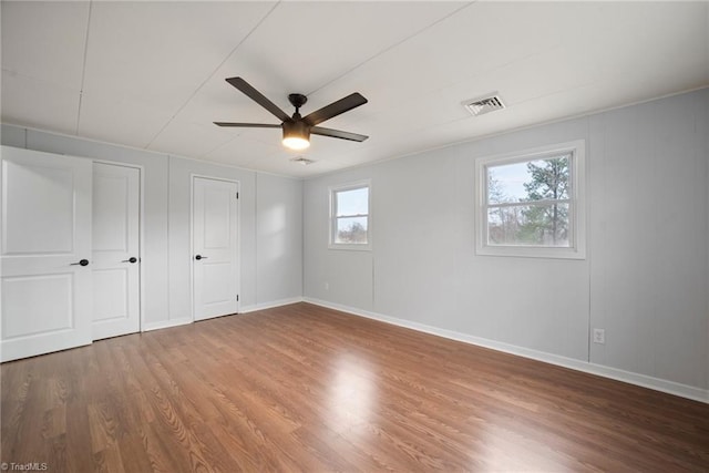 unfurnished bedroom featuring a ceiling fan, visible vents, baseboards, and wood finished floors