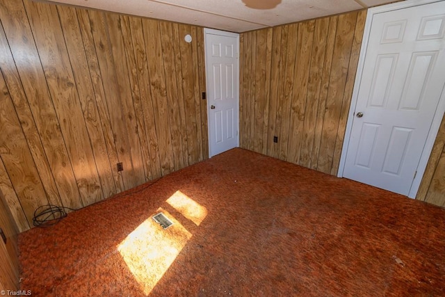 unfurnished room with visible vents, wood walls, and carpet floors