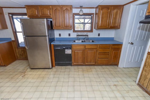 kitchen featuring light floors, black dishwasher, brown cabinets, freestanding refrigerator, and a sink