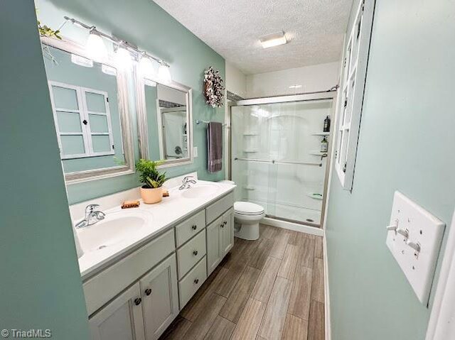 525 Bennett St, Mount Airy, NC 27030 - bathroom with toilet, a stall shower, double vanity, a textured ceiling, and wood finished floors