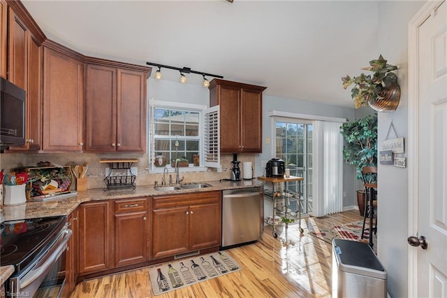 kitchen featuring light stone countertops, sink, stainless steel appliances, backsplash, and light wood-type flooring