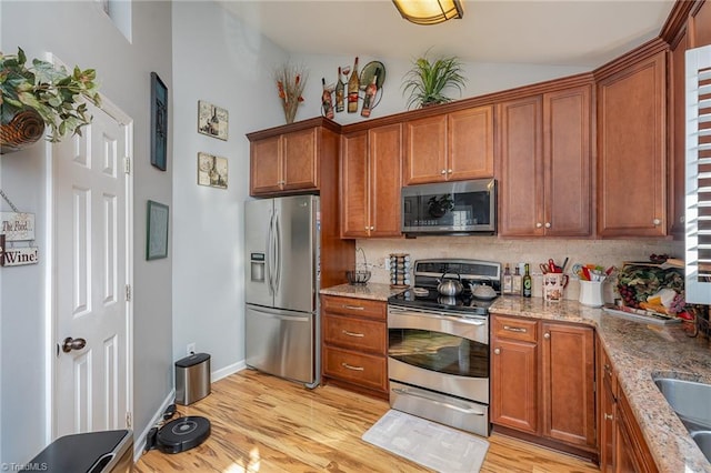 kitchen with light stone countertops, appliances with stainless steel finishes, and light hardwood / wood-style flooring